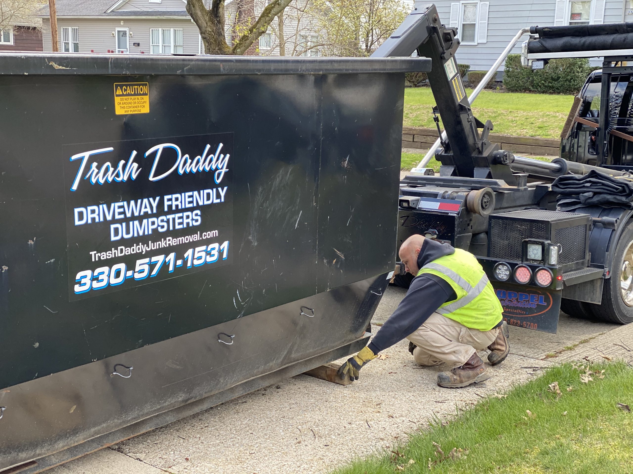 Trash Daddy Dumpster Checking Wood Under Dumpster in a Residential Driveway