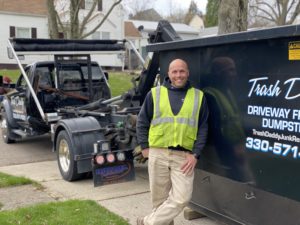 Trash Daddy owner Brian leaning against his truck delivering a dumpster to a residential home.